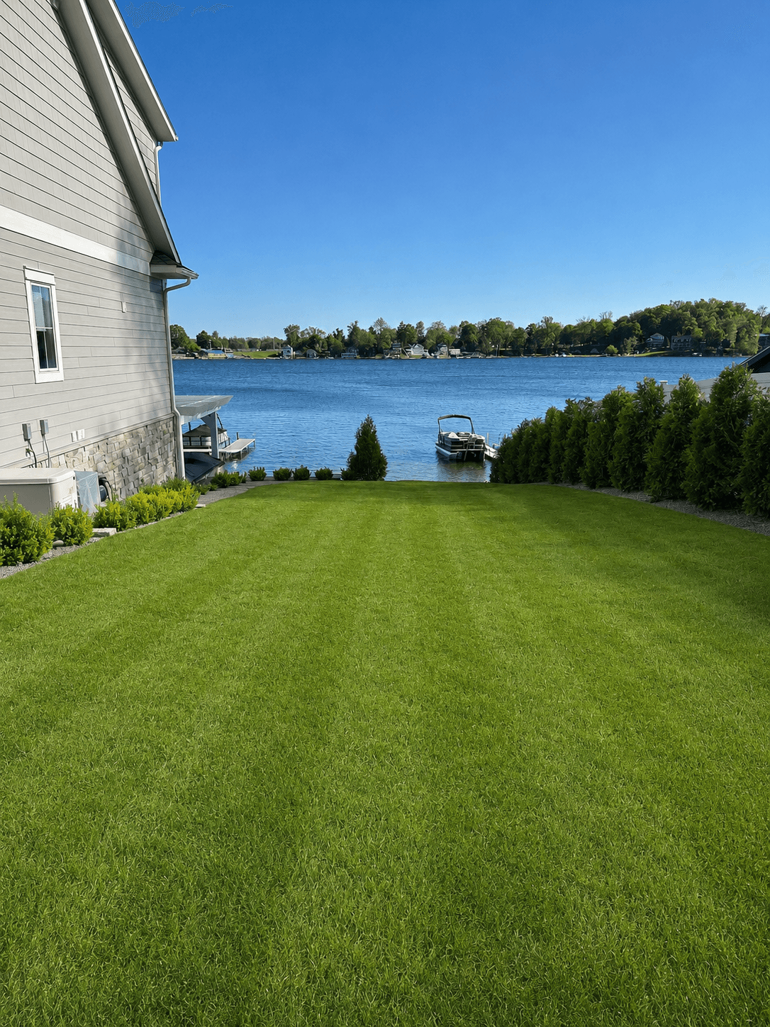 Lush lakefront lawn with pontoon boat and arborvitae hedge, Southwest Michigan