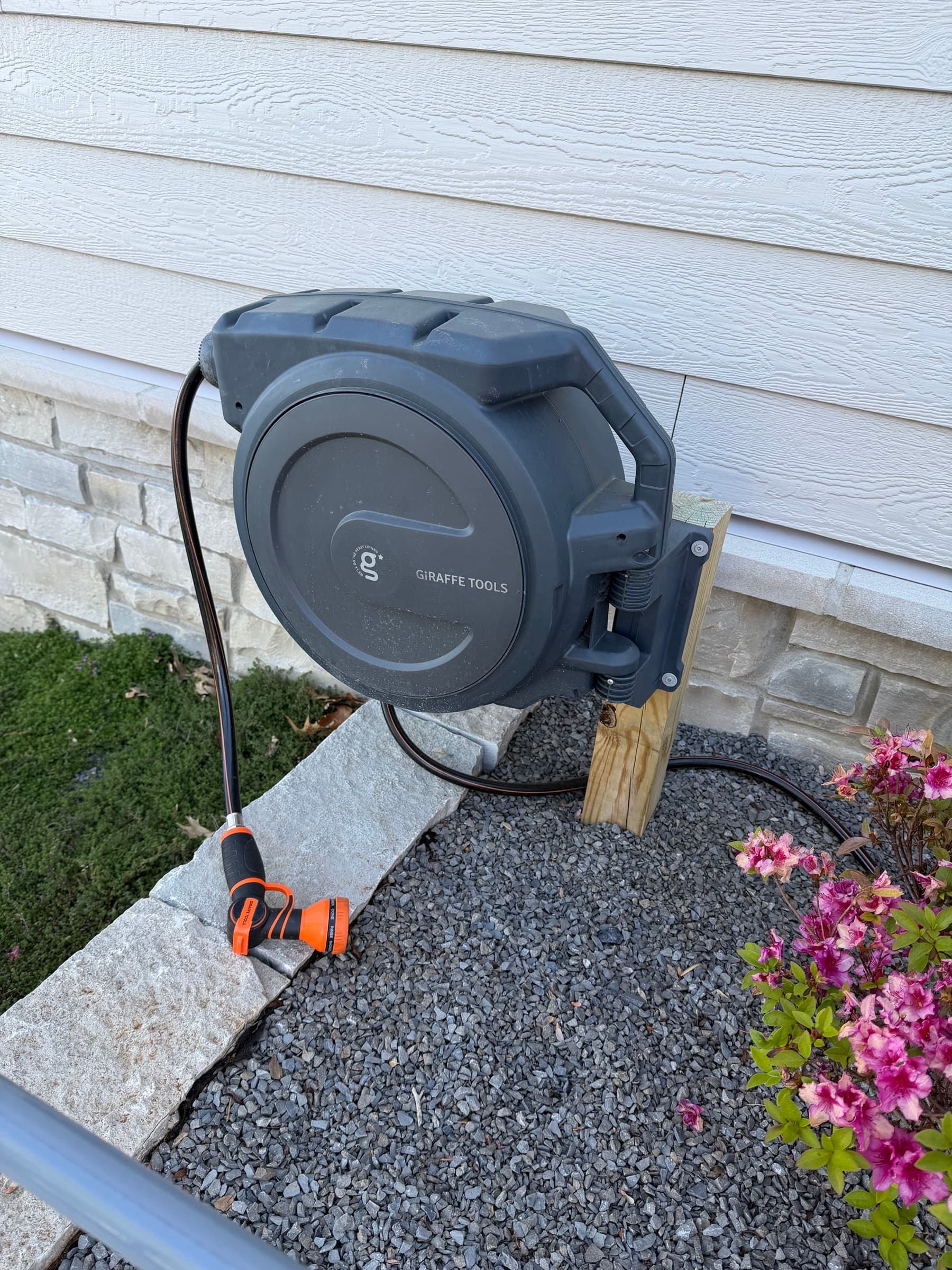 Retractable hose reel mounted to house exterior with stone and gravel drainage bed