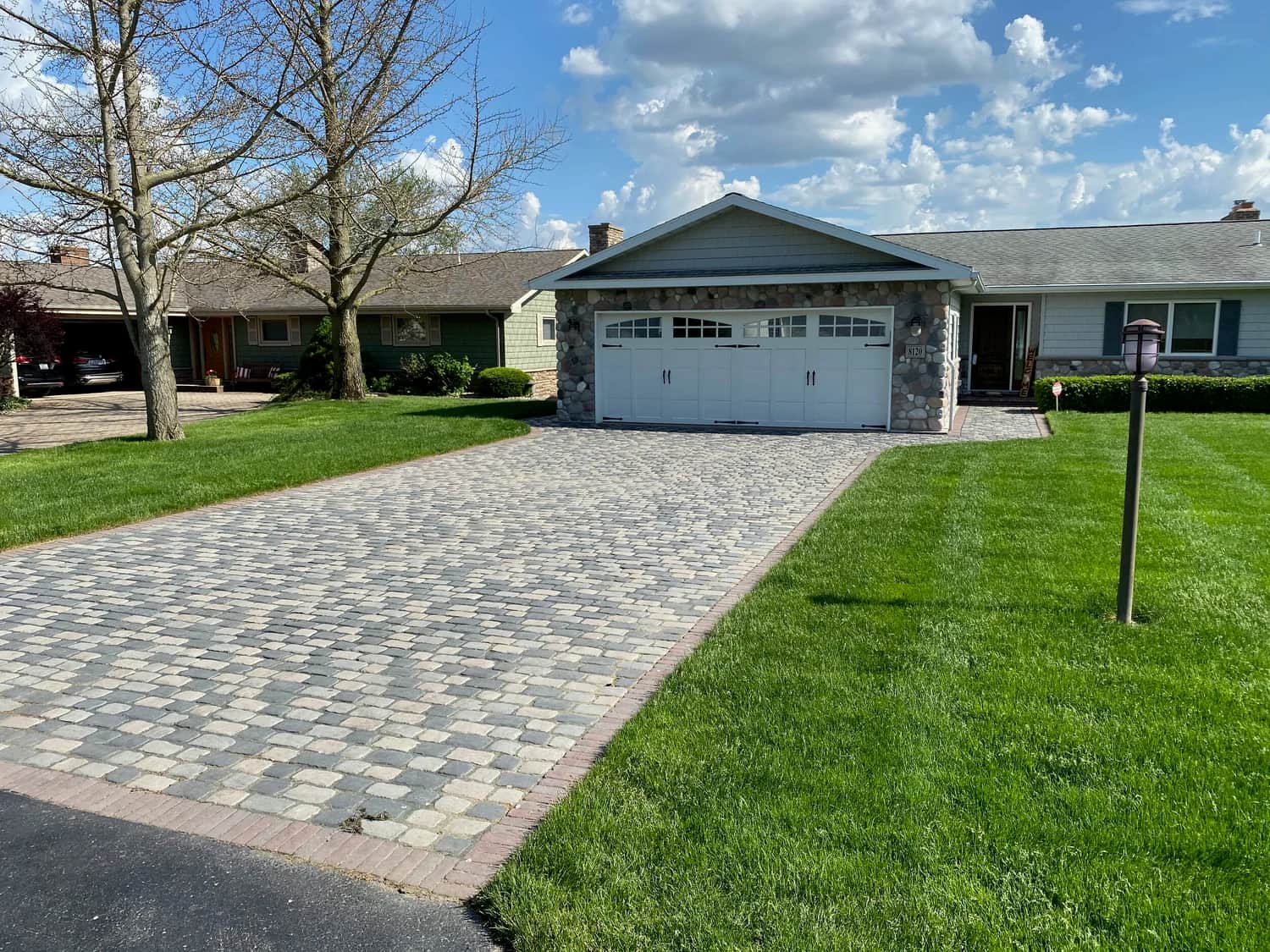Paver driveway with lush green lawn and blue sky